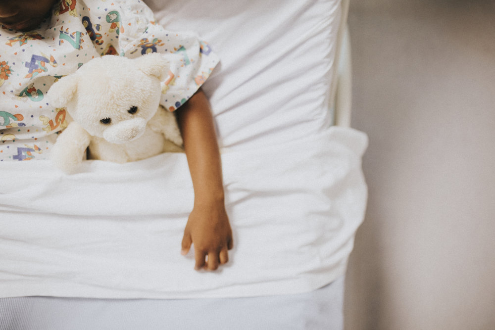 A child holding a teddy bear while resting in a hospital bed